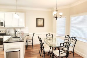 A modern kitchen with white cabinetry, a central island with a sink, and a dining area with a glass table and chairs.