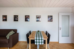 Uma área de refeições com mesa de madeira, cadeiras pretas, toalha de mesa xadrez e quatro quadros na parede.