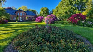 A large brick house with a well-maintained lawn and flowering bushes. - Apartment 'Haloi' with Private Terrace, Private Garden and Wi-Fi (Mittelangeln-Torsballig)