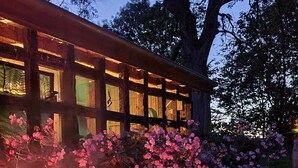 A building with a fire pit in the foreground and a garden with pink flowers. - Apartment 'Haloi' with Private Terrace, Private Garden and Wi-Fi (Mittelangeln-Torsballig)