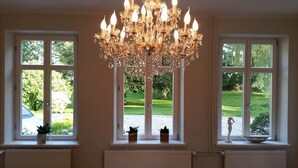 A room with three windows, a chandelier, and potted plants. - Apartment 'Haloi' with Private Terrace, Private Garden and Wi-Fi (Mittelangeln-Torsballig)