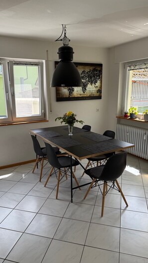 A dining area with a table, chairs, a pendant light, a world map artwork, and a window with a view.