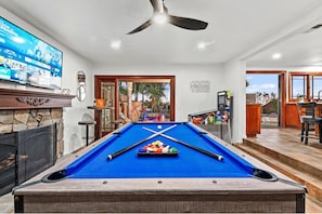 A pool table with a blue felt surface, a television mounted on the wall, and a ceiling fan.