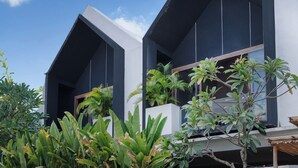 A modern building with a flat roof, large windows, and a concrete facade. There is a paved area in front with a wooden door. - Liminal Palace Villa 1 by Betterplace (Canggu)