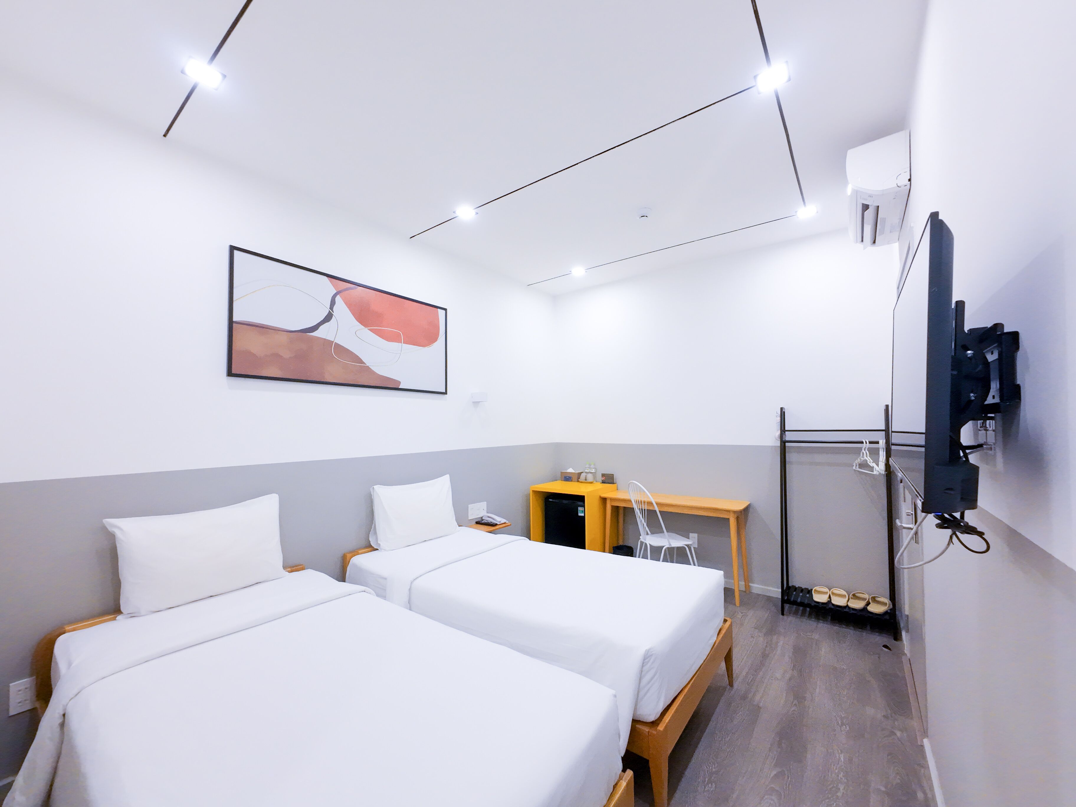 A hotel room with two beds, a desk, a chair, a TV, and a shoe rack.