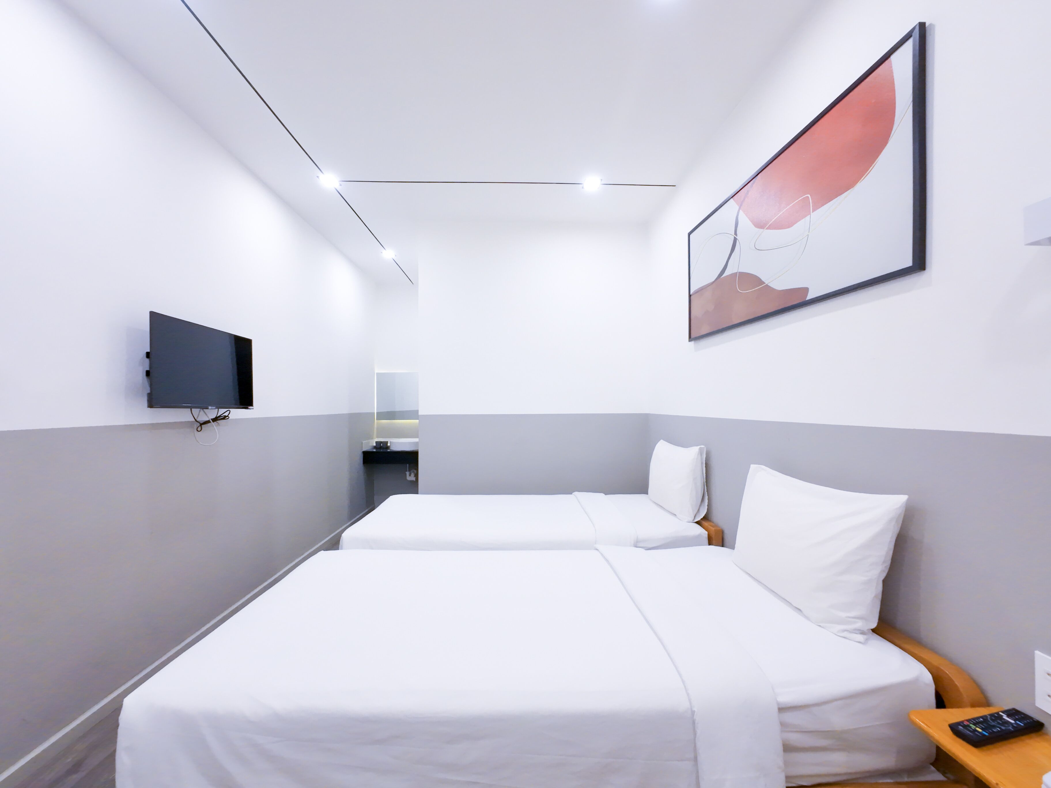 A hotel room with two single beds, a flat-screen TV mounted on the wall, and a small bedside table with a remote control.