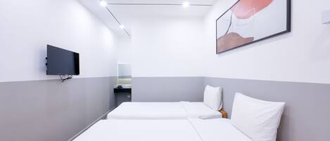 A hotel room with two single beds, a flat-screen TV mounted on the wall, and a small bedside table with a remote control.