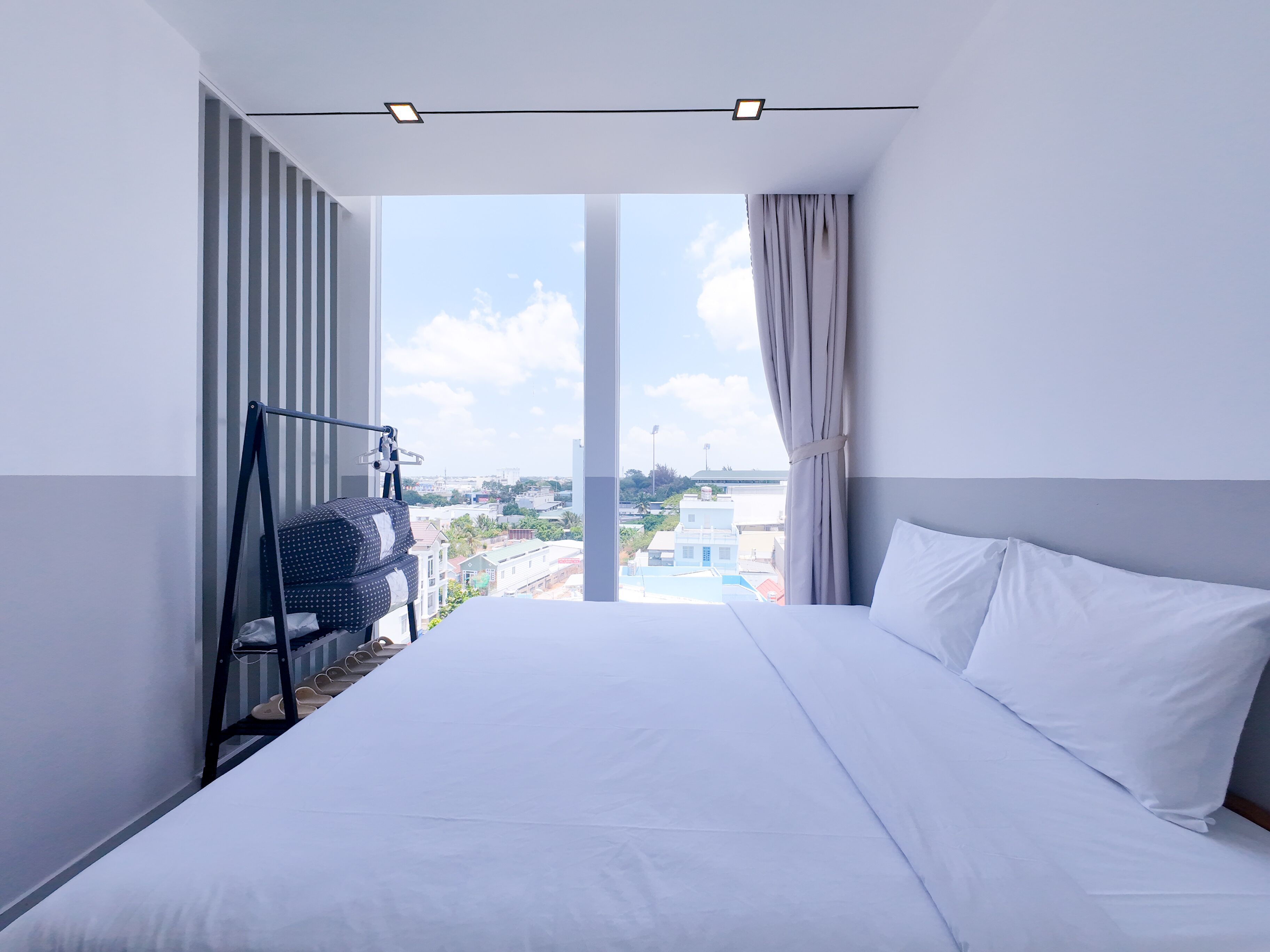A hotel room with a large bed, a view of the cityscape, and a balcony with a chair.