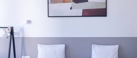 Habitación de hotel con dos camas, un cuadro en la pared, un teléfono en una mesita de noche y un zapatero.