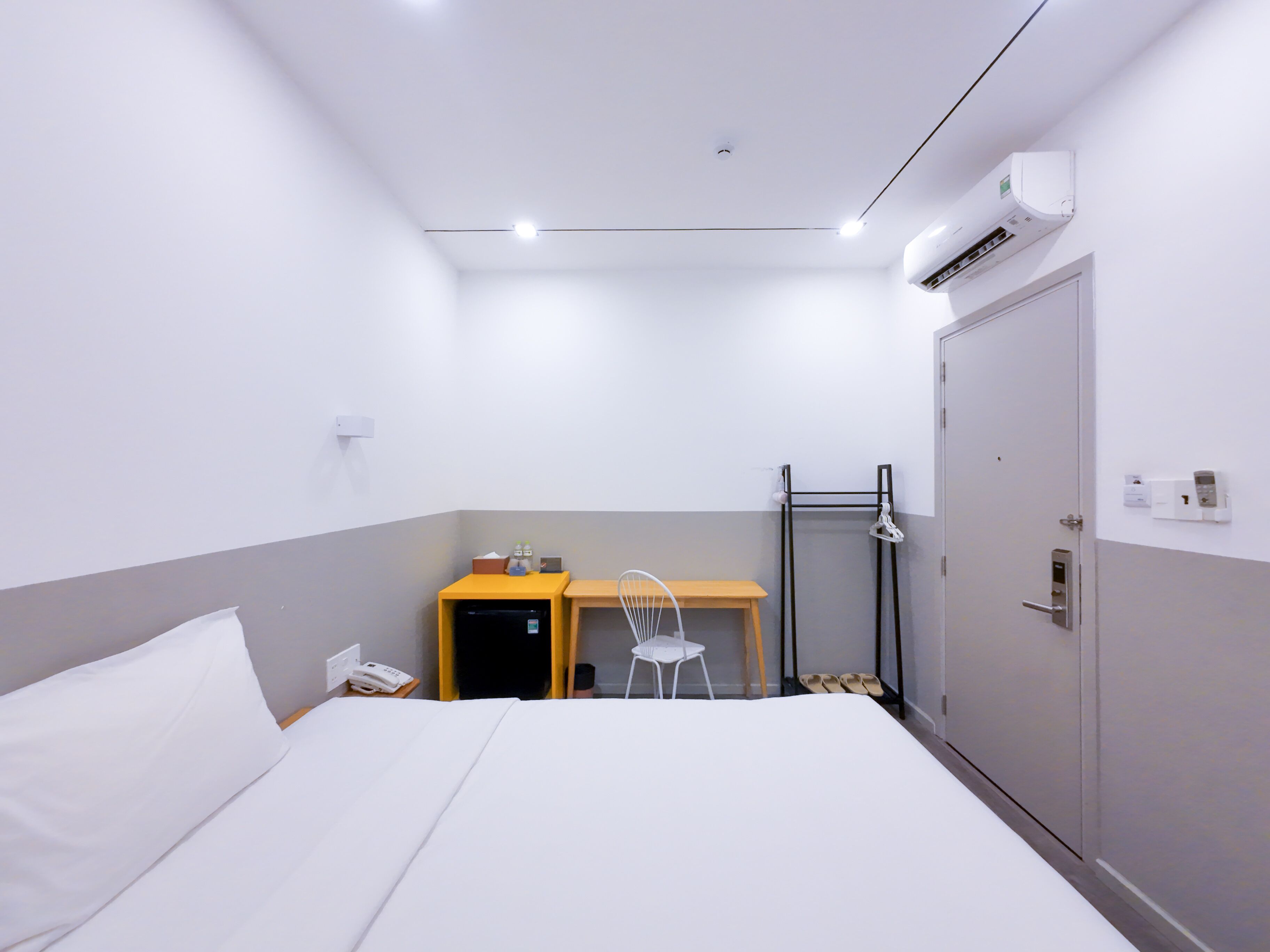 A hotel room with a bed, a desk, a chair, a wardrobe, and an air conditioning unit.