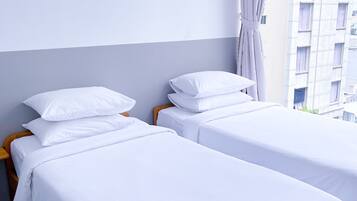 Twee eenpersoonsbedden met witte lakens in een hotelkamer.