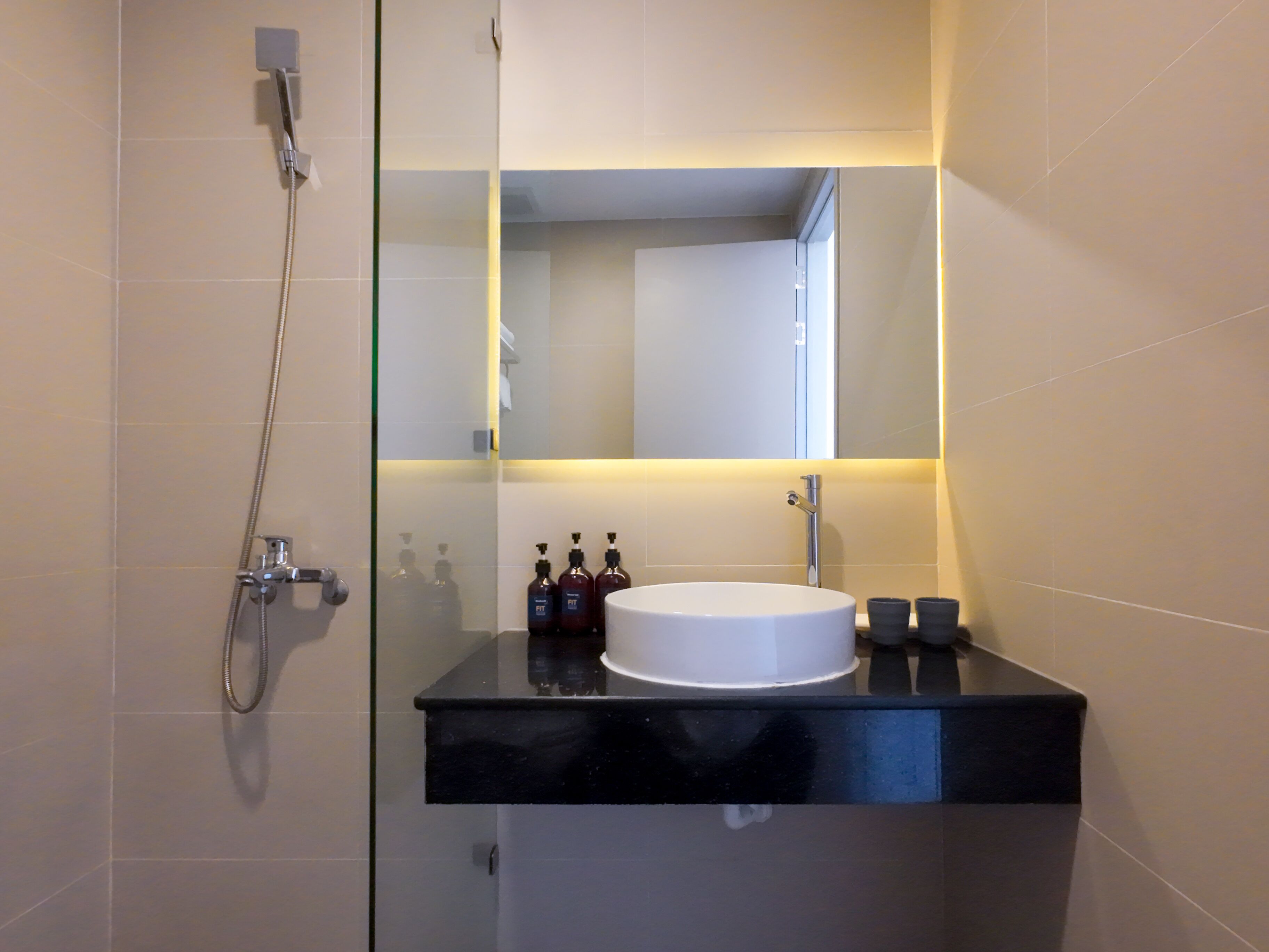 Une salle de bain moderne avec une douche à l’italienne en verre, un plan de toilette noir et un lavabo blanc.