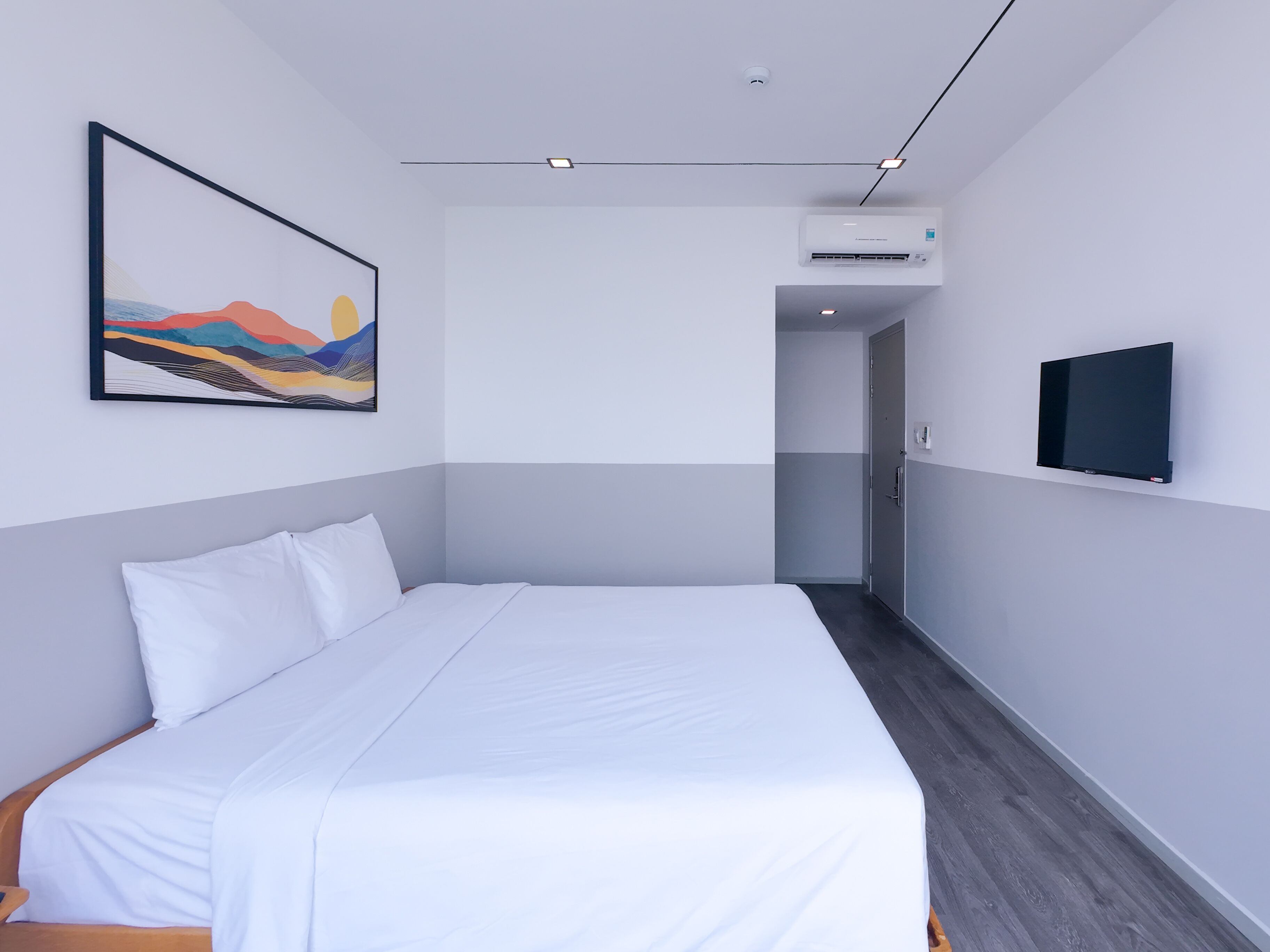 A modern hotel room with a large bed, a mounted TV, and an air conditioning unit.