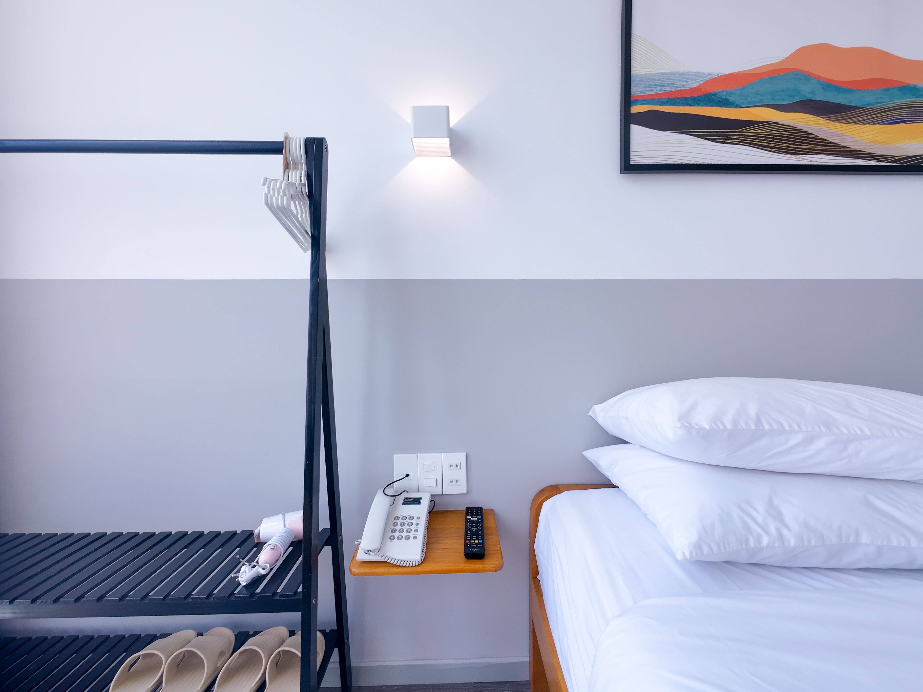 Ein Hotelzimmer mit Etagenbett, Nachttisch, Telefon und Fernbedienung, einem Paar Hausschuhen und einem Bild an der Wand.