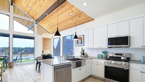 A modern kitchen with a large island, stainless steel appliances, and a view of the outdoors. - Cozy, Hill Country Cabin! (New Braunfels)