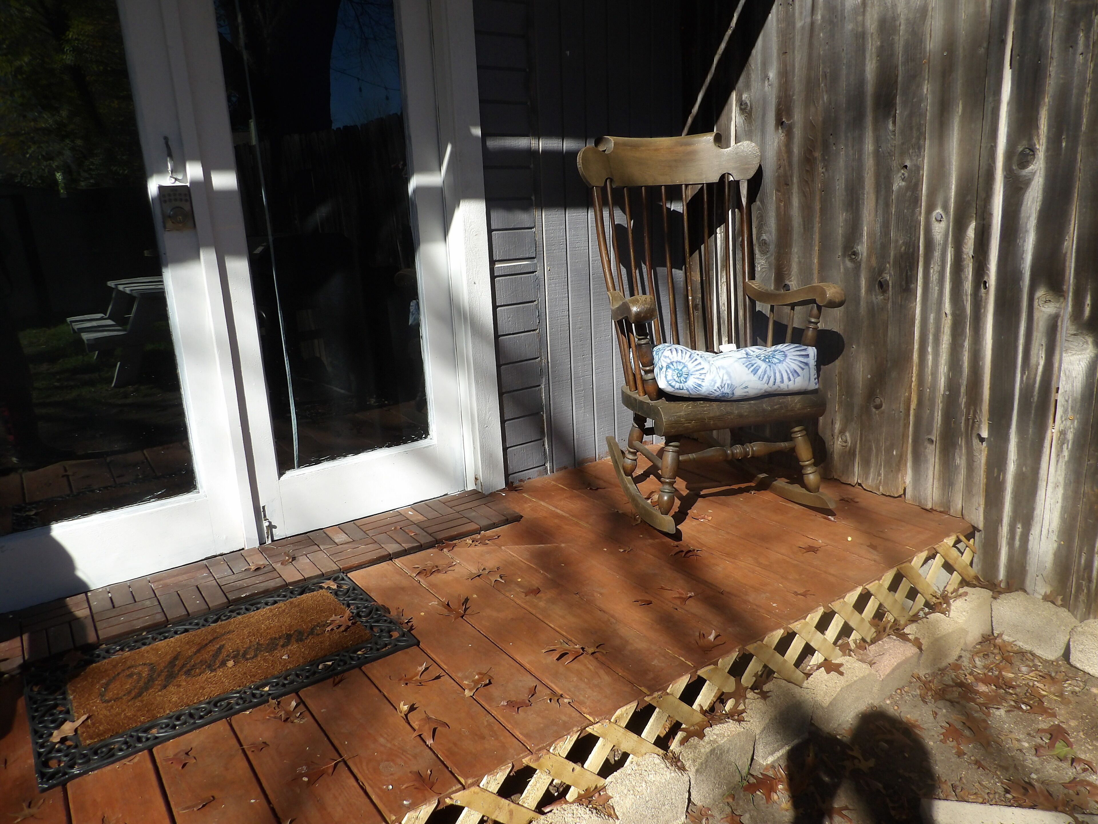 A wooden porch with a rocking chair and a doormat.