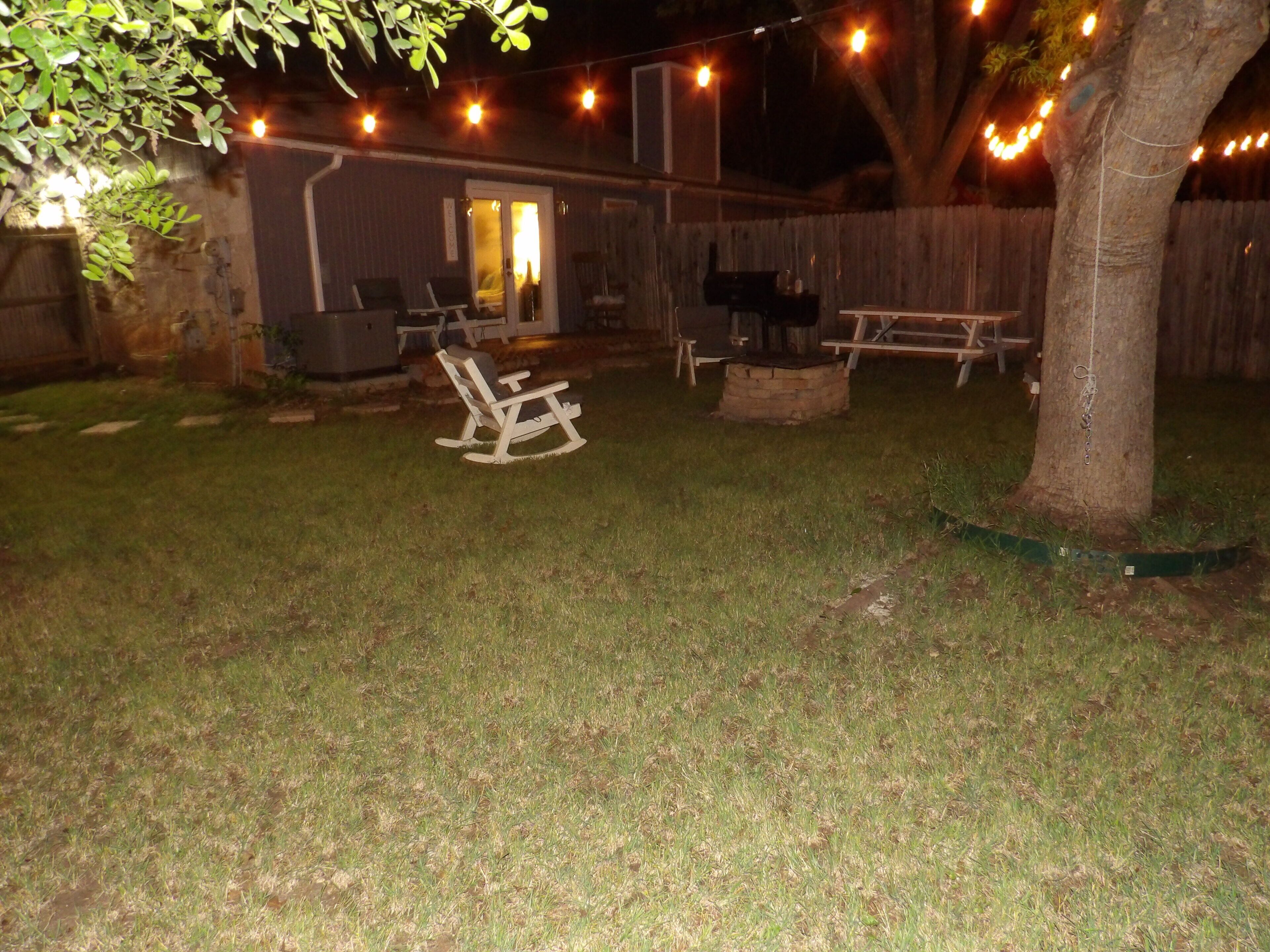 Un jardin avec un fauteuil à bascule en bois, un barbecue et des guirlandes lumineuses.