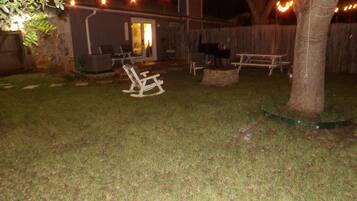 Un jardin avec un fauteuil à bascule en bois, un barbecue et des guirlandes lumineuses.