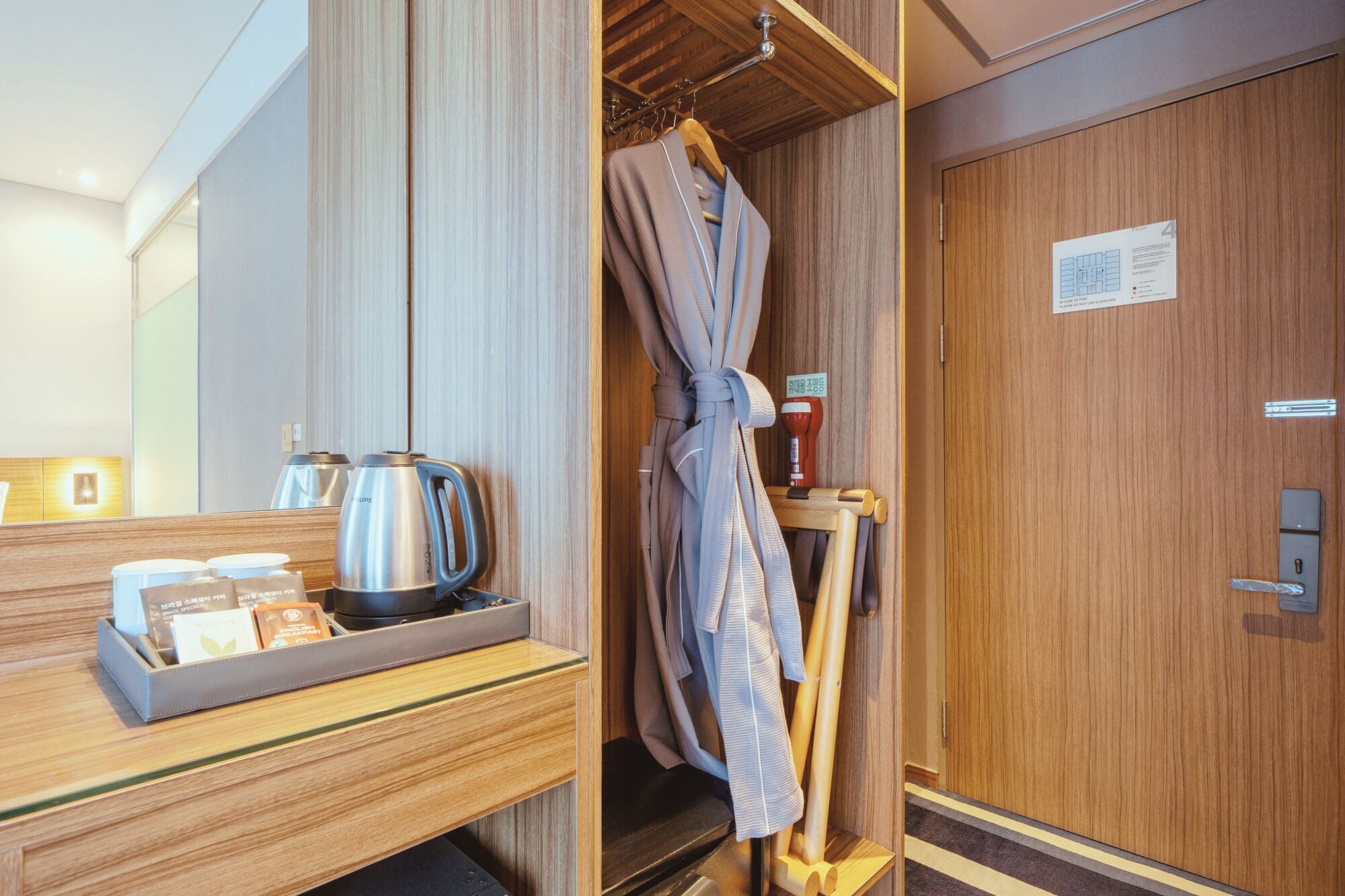 Habitación de hotel con un armario de madera, una bata colgada en un perchero, una bandeja con un hervidor y bolsitas de té, y un cartel que indica el número de habitación 4.