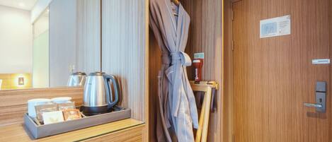 Habitación de hotel con un armario de madera, una bata colgada en un perchero, una bandeja con un hervidor y bolsitas de té, y un cartel que indica el número de habitación 4.