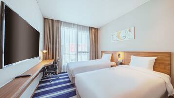 Een hotelkamer met twee bedden, een televisie, een bureau met stoel, een lamp en een raam met gordijnen.