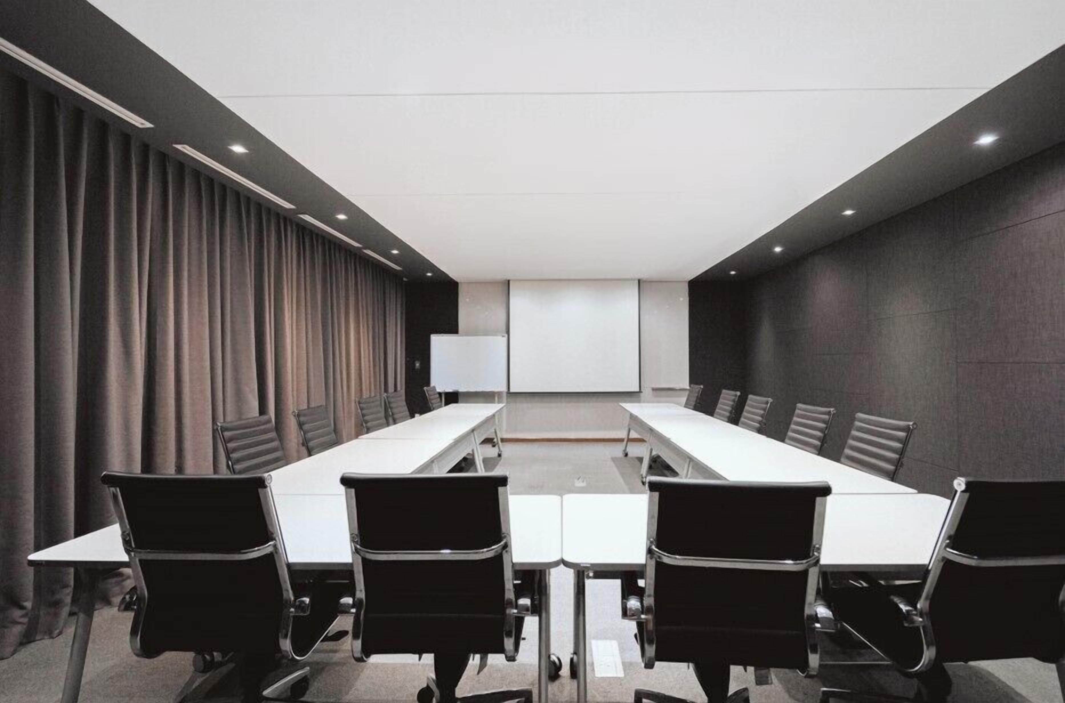 Une salle de conférence équipée d’une longue table et de chaises, d’un tableau blanc et d’un écran de projection.