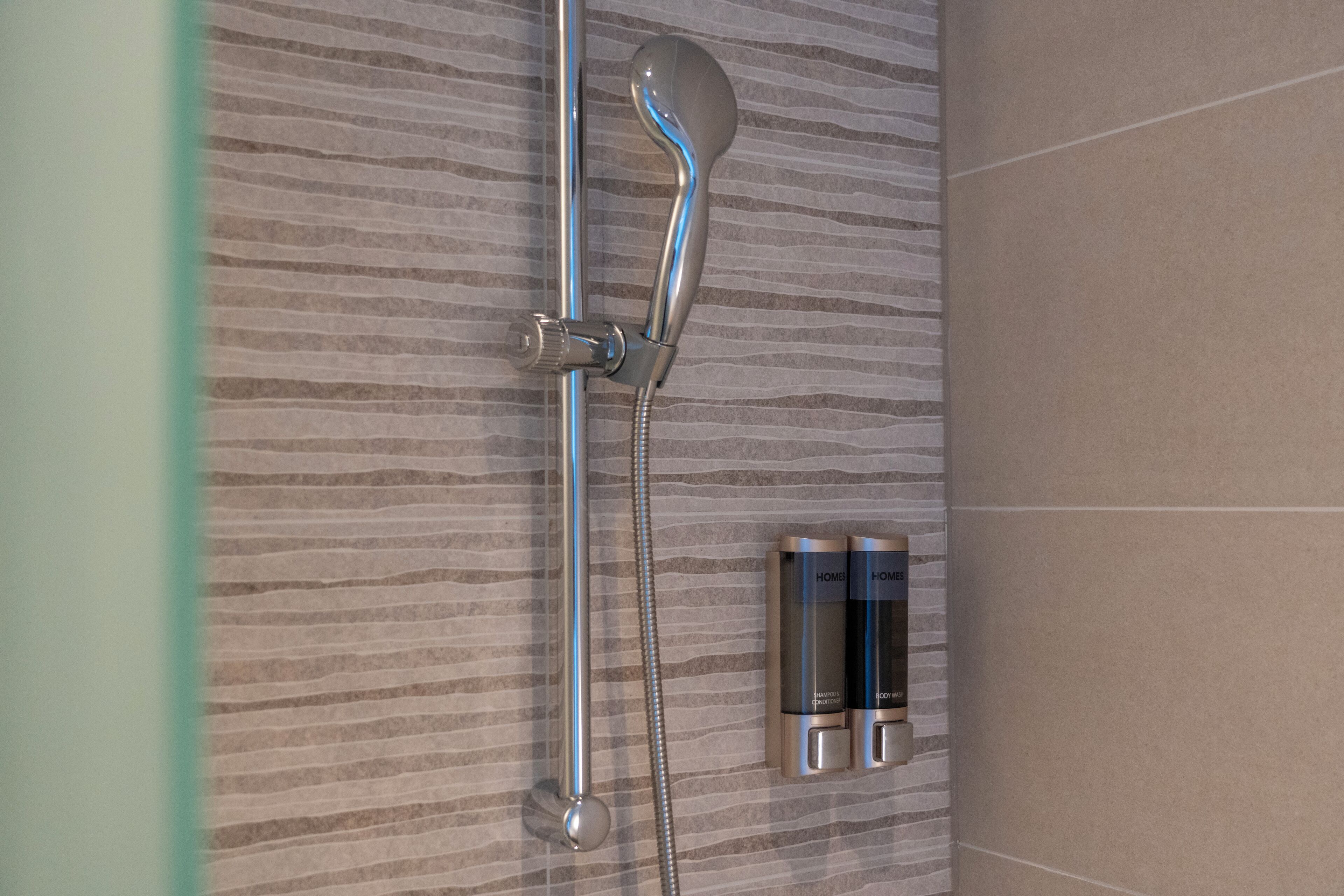 A shower with a handheld showerhead and a wall-mounted control panel.