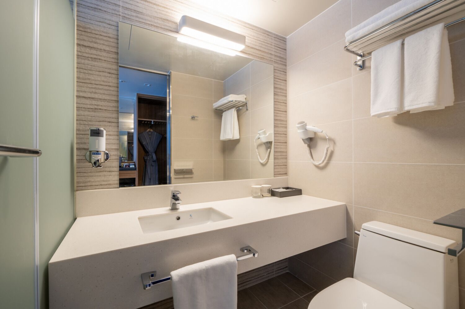 A modern bathroom with a large mirror, a sink, a toilet, and a hairdryer mounted on the wall.