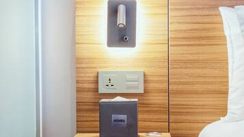 A hotel room with a wooden panel wall, a bedside table with a box labeled "HOMES", a light switch, and a power outlet.