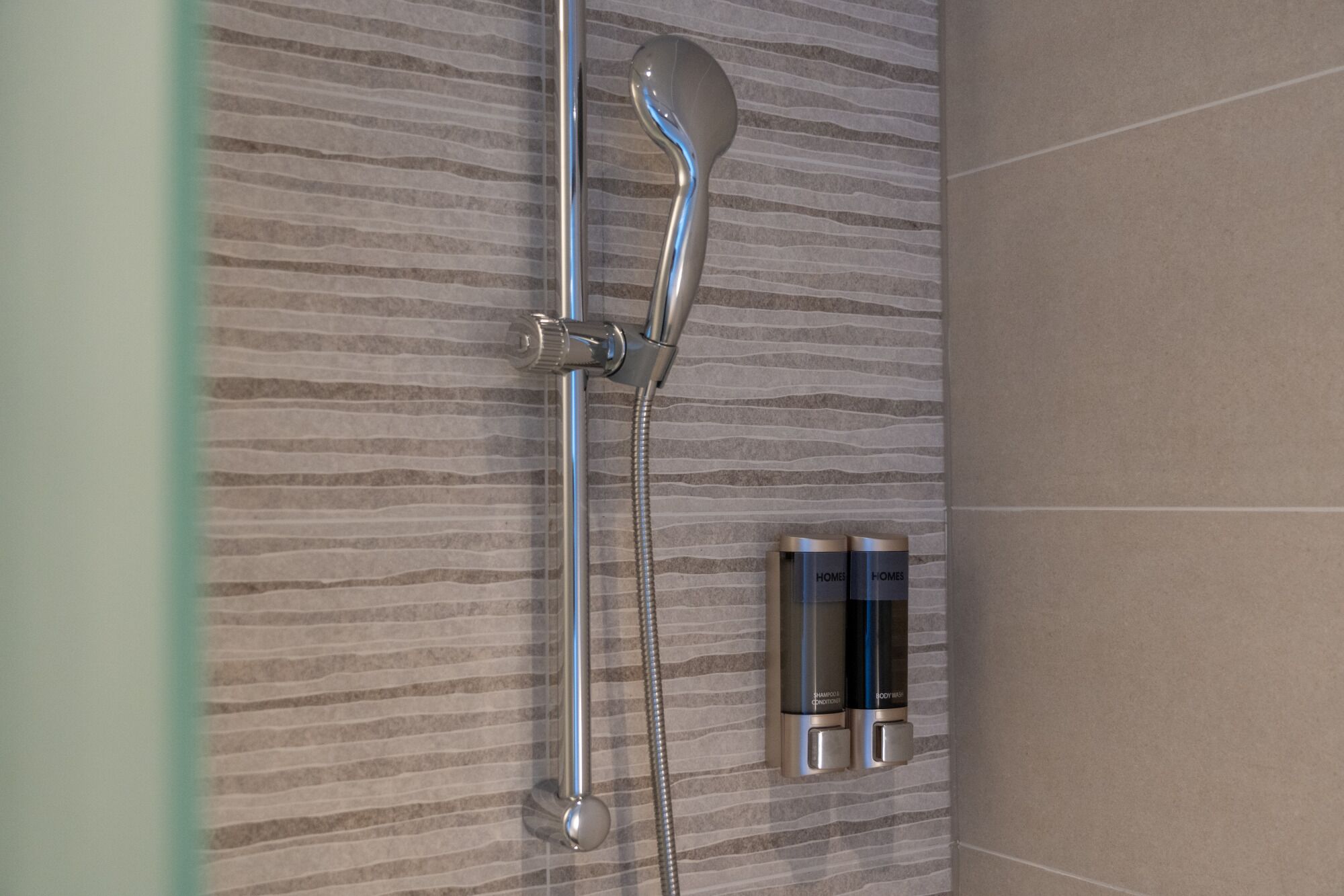 A shower with a handheld showerhead and a wall-mounted control panel.