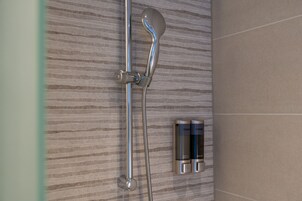 A shower with a handheld showerhead and a wall-mounted control panel.