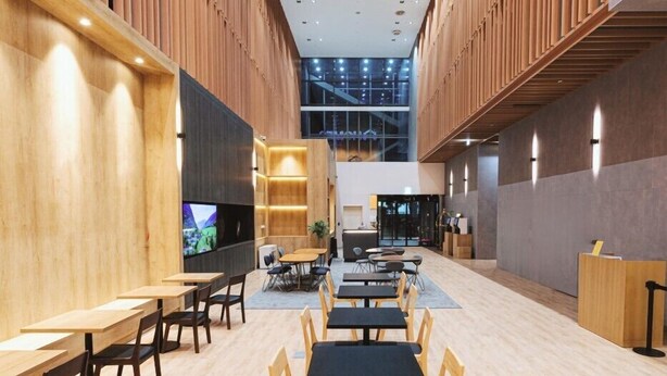 A modern indoor space with wooden panel walls, multiple seating areas, and a large screen displaying a sports event. - HOMES Stay Suwon (Suwon)