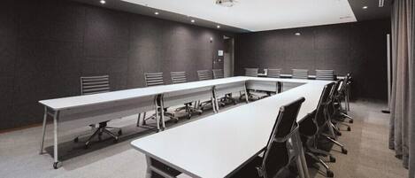 Une salle de conférence avec une longue table et des chaises, des murs sombres et un éclairage encastré.