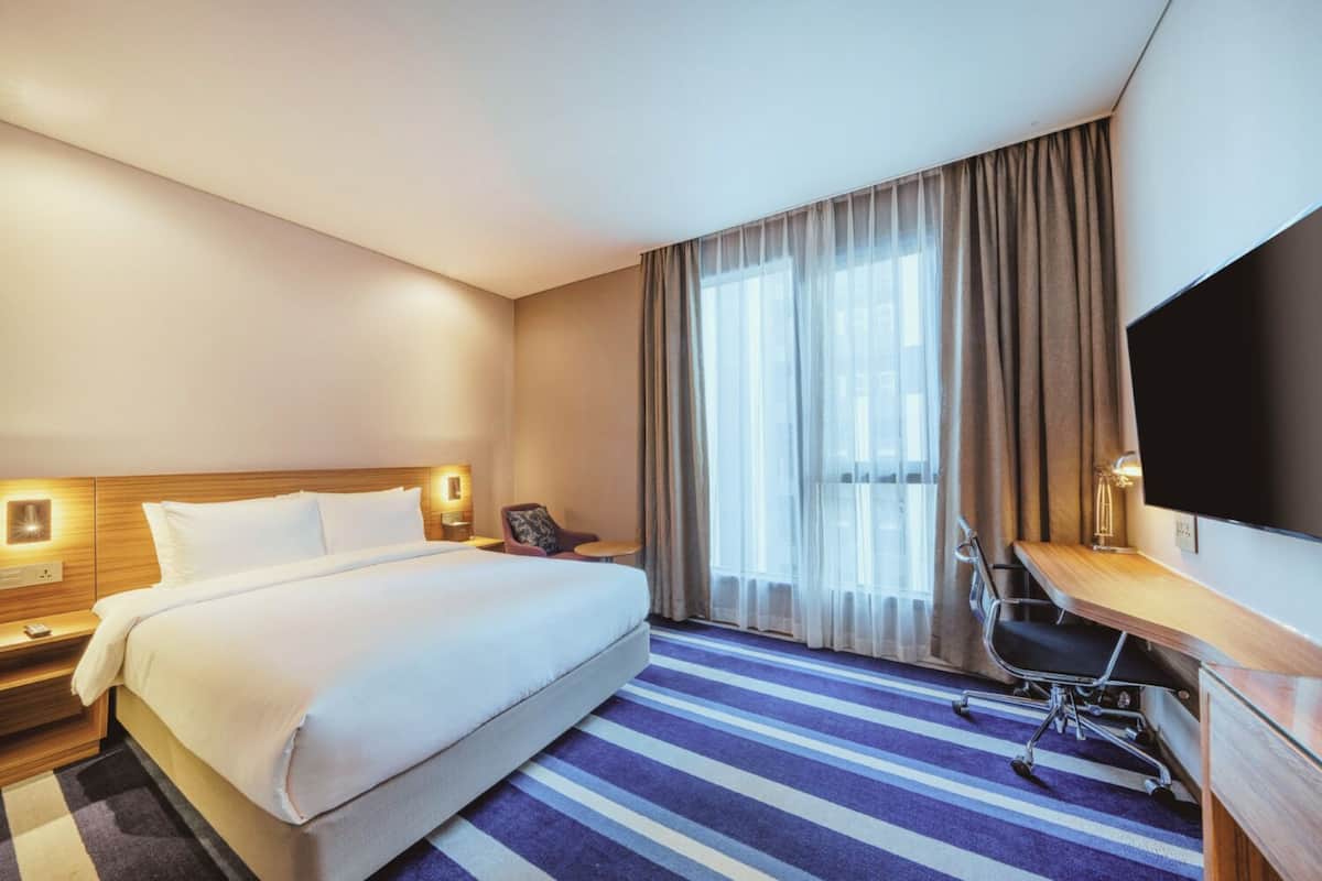 A hotel room with a large bed, a desk, a chair, a TV, and a window with curtains.