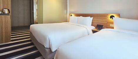 A hotel room with two beds, a wooden headboard, a nightstand with a phone, and a striped carpet.