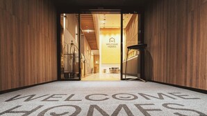 A hotel entrance with a 'Welcome Homes' sign, a reception desk, and a carpet with the hotel's name. - HOMES Stay Suwon (Suwon)