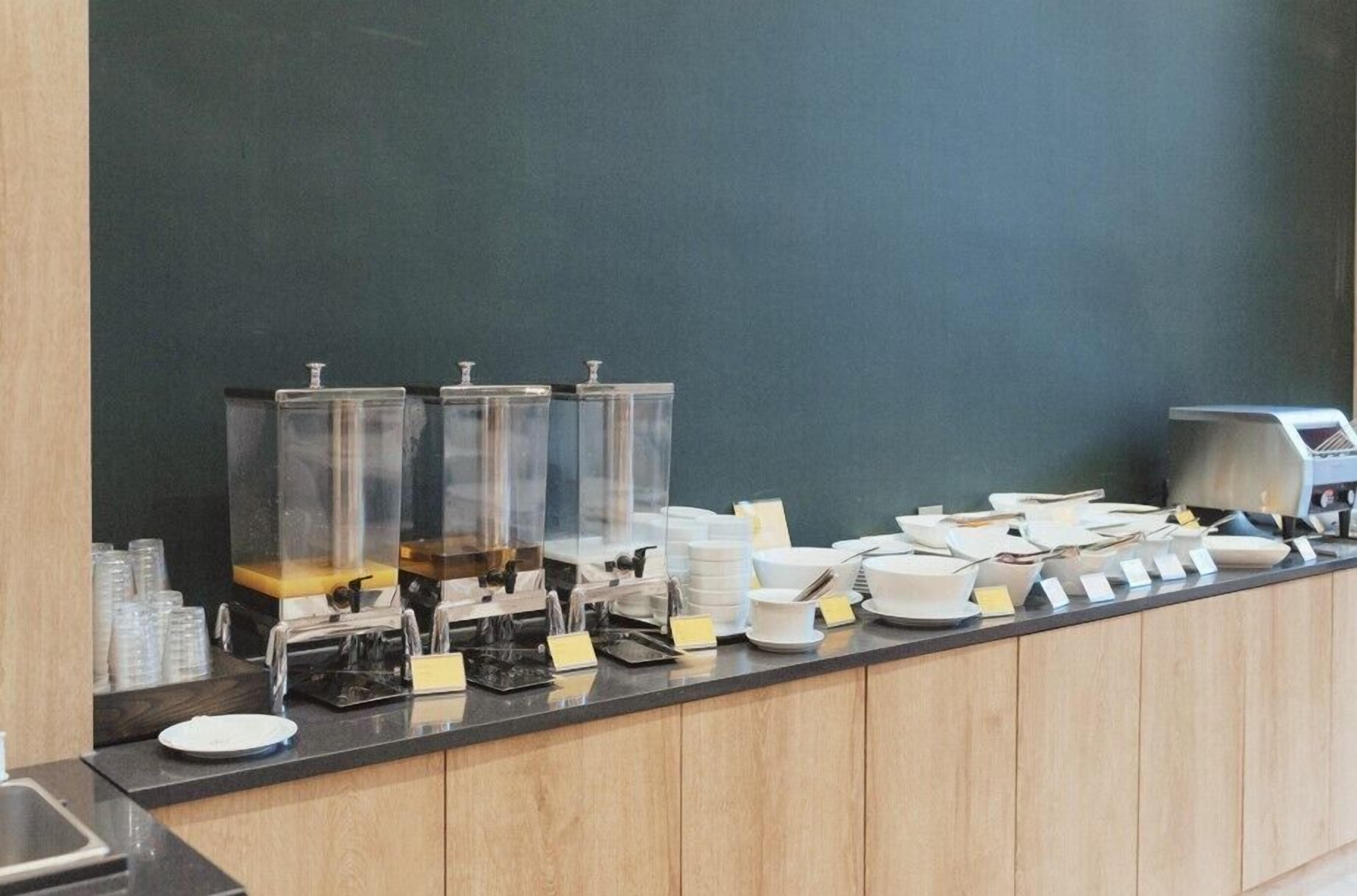 A buffet counter with clear glass dispensers, white plates, and a coffee machine.