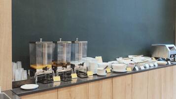A buffet counter with clear glass dispensers, white plates, and a coffee machine.