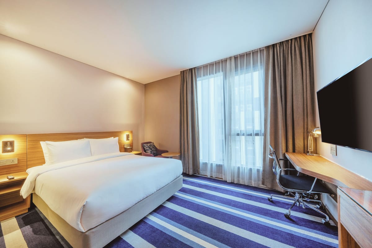 A hotel room with a large bed, a desk, a chair, and a TV.