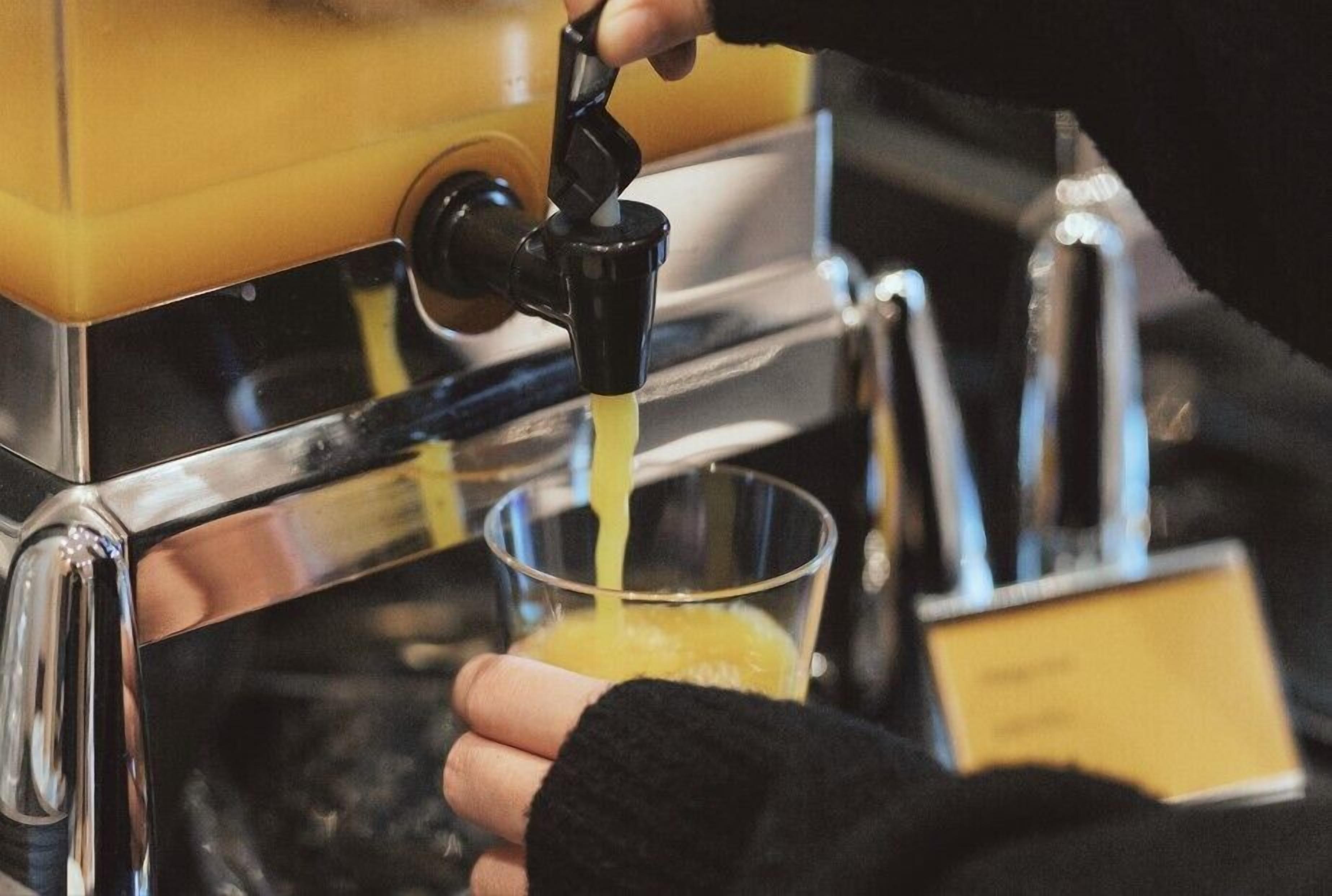 A hand holding a glass under a coffee machine dispensing coffee.