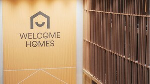 A modern interior with a 'Welcome Homes' sign, wooden flooring, and a row of tables and chairs. - HOMES Stay Suwon (Suwon)