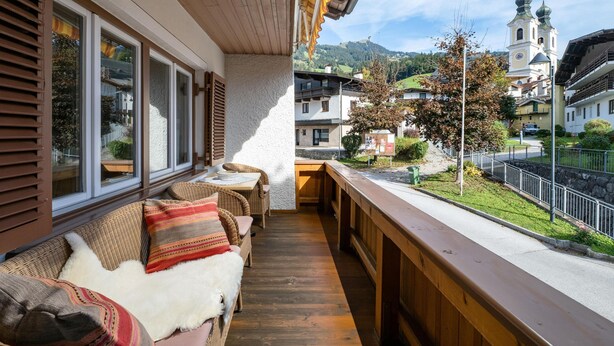 A wooden deck with wicker furniture and a view of a church with two domes. - Spacious holiday home in the centre (Hopfgarten im Brixental)