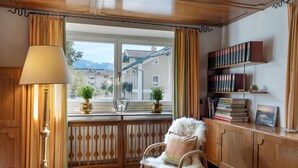 A cozy room with a wooden cabinet, a bookshelf, a chair with a fluffy cushion, a floor lamp, and a window with curtains. - Spacious holiday home in the centre (Hopfgarten im Brixental)