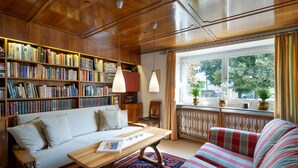 A cozy living room with a sofa, a coffee table, a striped armchair, a bookshelf, and a window with a view of trees. - Spacious holiday home in the centre (Hopfgarten im Brixental)