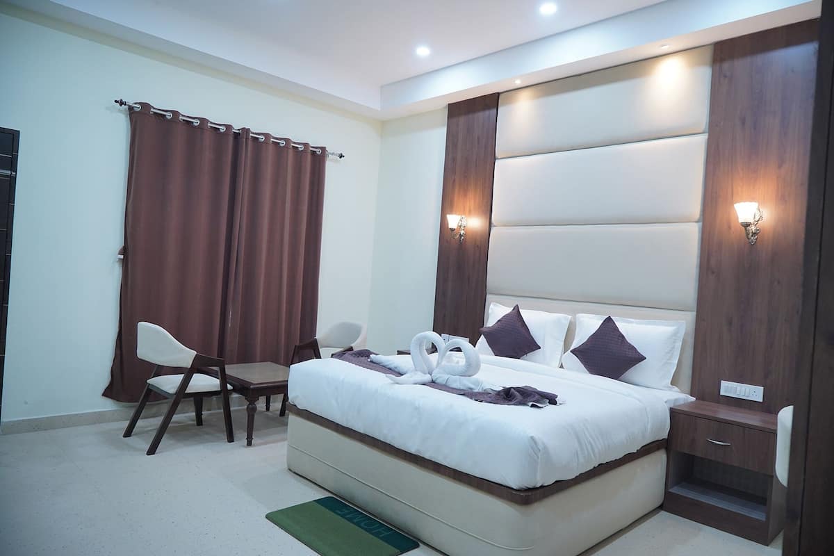 A hotel room with a large bed, two bedside tables, a chair, a desk, and a curtain.