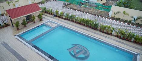 Una piscina con un logo al centro, circondata da piante in vaso e un solarium piastrellato.