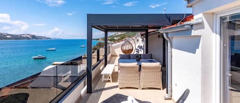 A balcony with a view of the sea, wicker furniture, and a table.