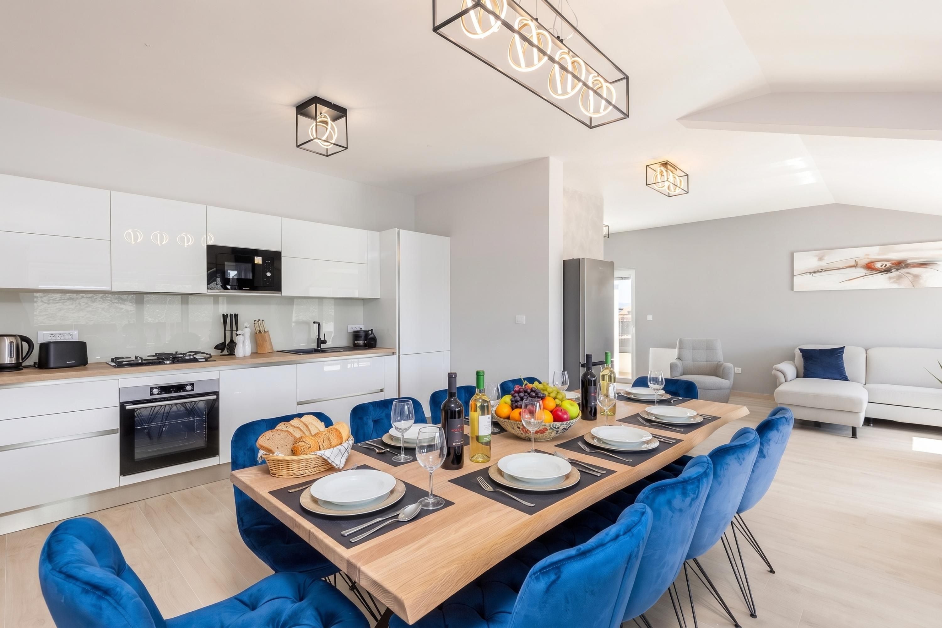 Una cocina moderna con armarios blancos, microondas integrado y comedor con mesa de madera para cuatro.