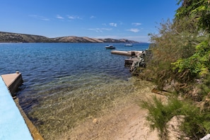A clear waterfront with a pier extending into calm waters, surrounded by hills and sparse vegetation. - Family Resort Santa Maria II Penthouse (Novalja)