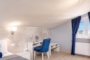 A bedroom with a bed, a desk, a chair, a mirror, and a window with curtains.